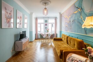 A room with a wooden floor, a yellow sofa, a TV on a cabinet, and a large abstract painting on the wall. - 4 People - Designer Apartment (Leipzig)