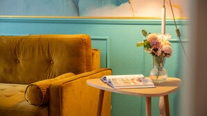 A room with a yellow sofa, a small round table with a magazine, and a vase with flowers.