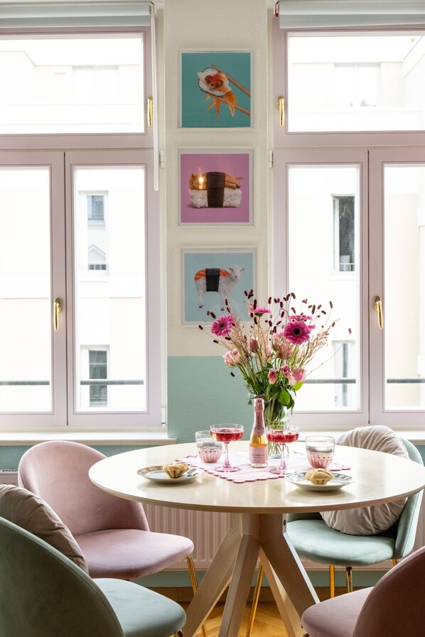 A dining area with a round table, pink chairs, and a vase with flowers.