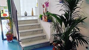 Uma escadaria com degraus de mármore leva a um patamar, cercado por plantas em vasos e um relógio na parede.