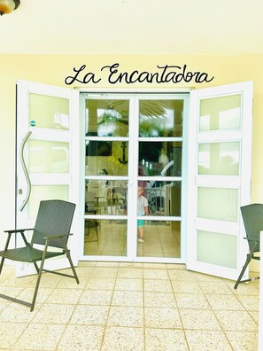 Habitación con un gran ventanal de vidrio con la leyenda "La Encantadora", que incluye dos sillones de mimbre y piso de baldosas.