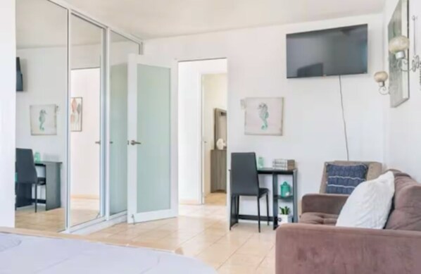Ein modernes Wohnzimmer mit einer Couch, einem an der Wand montierten Fernseher und einem Essbereich mit Tisch und Stühlen.