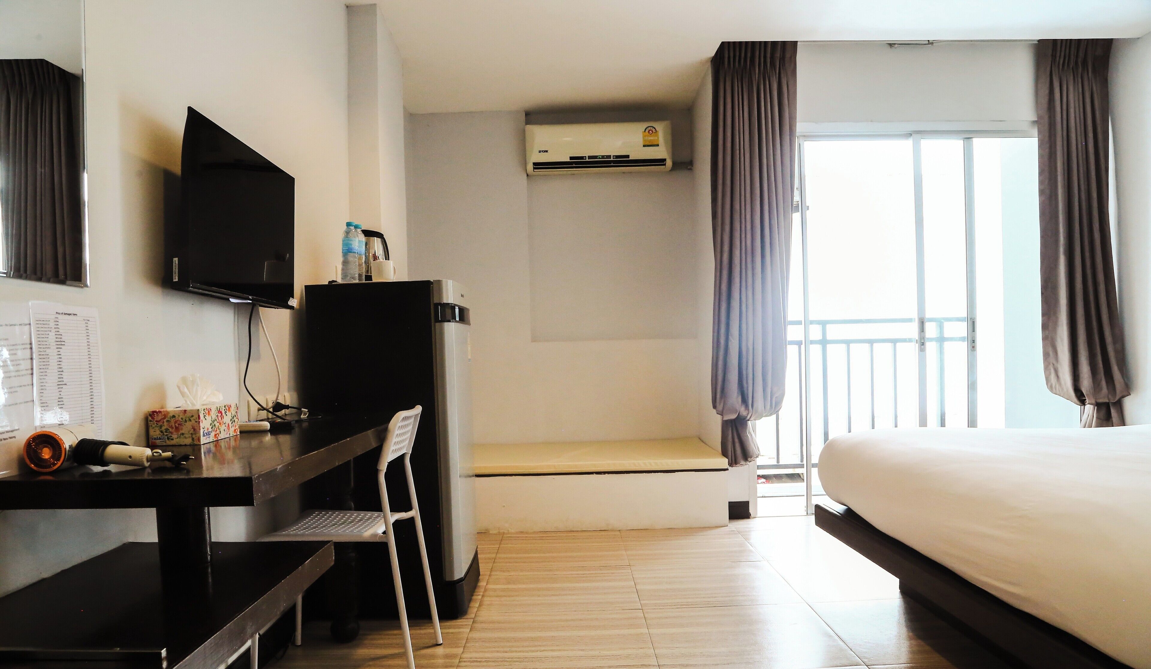 Ein Hotelzimmer mit Bett, Schreibtisch mit Stuhl, Fernseher, Klimaanlage und einem Fenster mit Vorhängen.