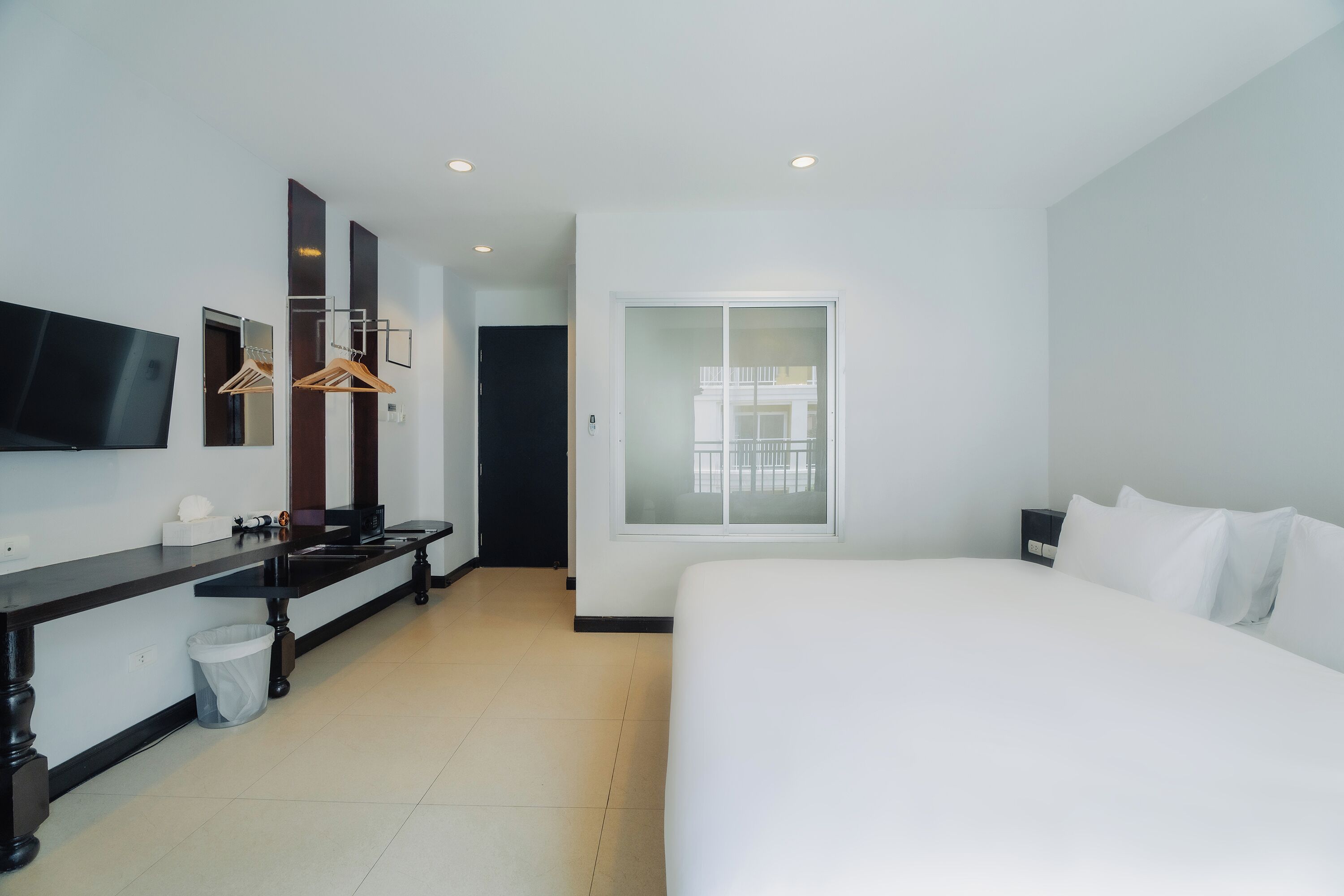 Une chambre d’hôtel moderne dotée d’un grand lit, d’un téléviseur à écran plat fixé au mur, d’un petit bureau avec une chaise et d’une fenêtre donnant sur un balcon.
