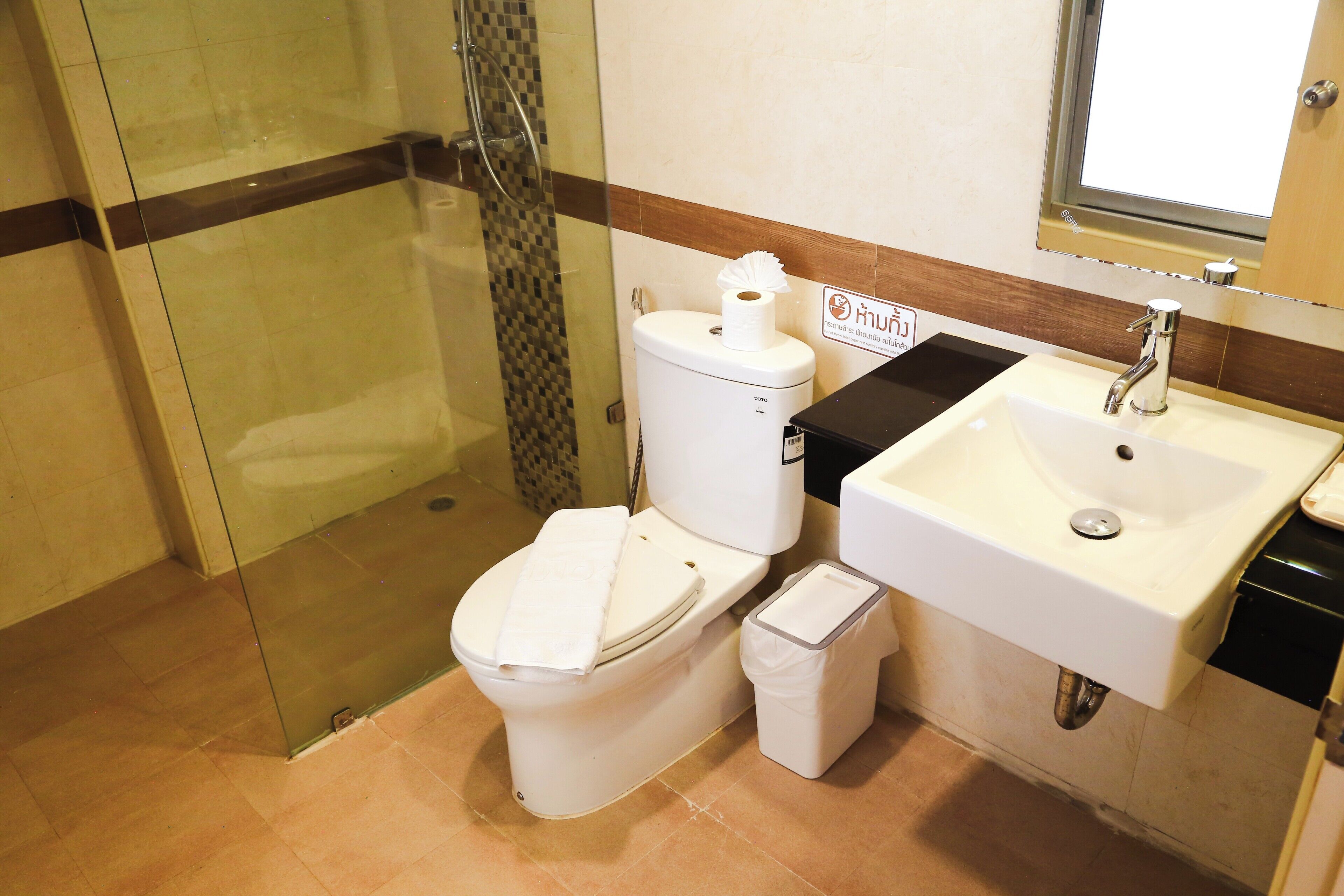 A bathroom with a glass shower enclosure, a toilet, a sink, and a trash bin.