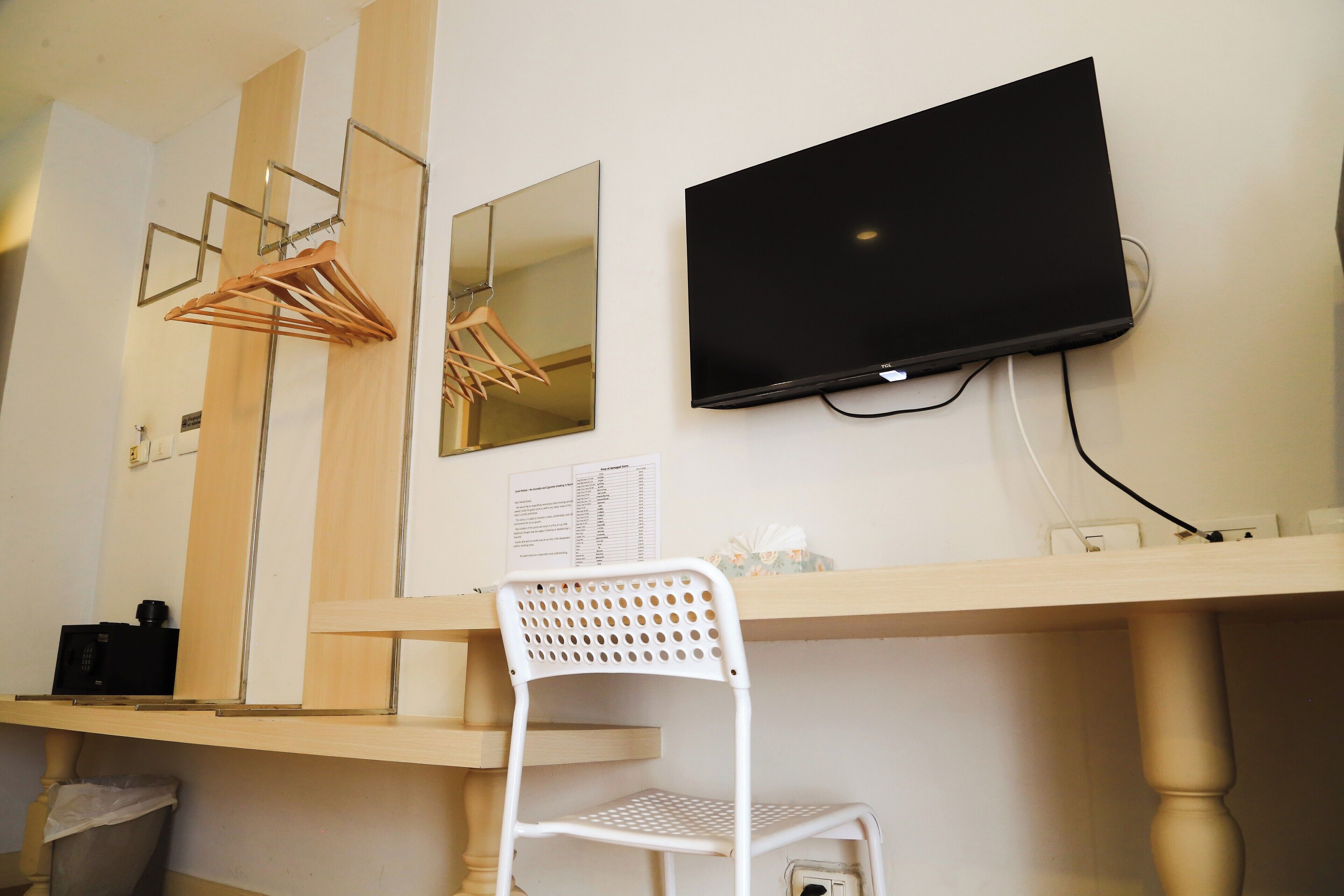 Ein Zimmer mit einem an der Wand befestigten Flachbildfernseher, einem Holztisch, einem weißen Stuhl und einem Spiegel.