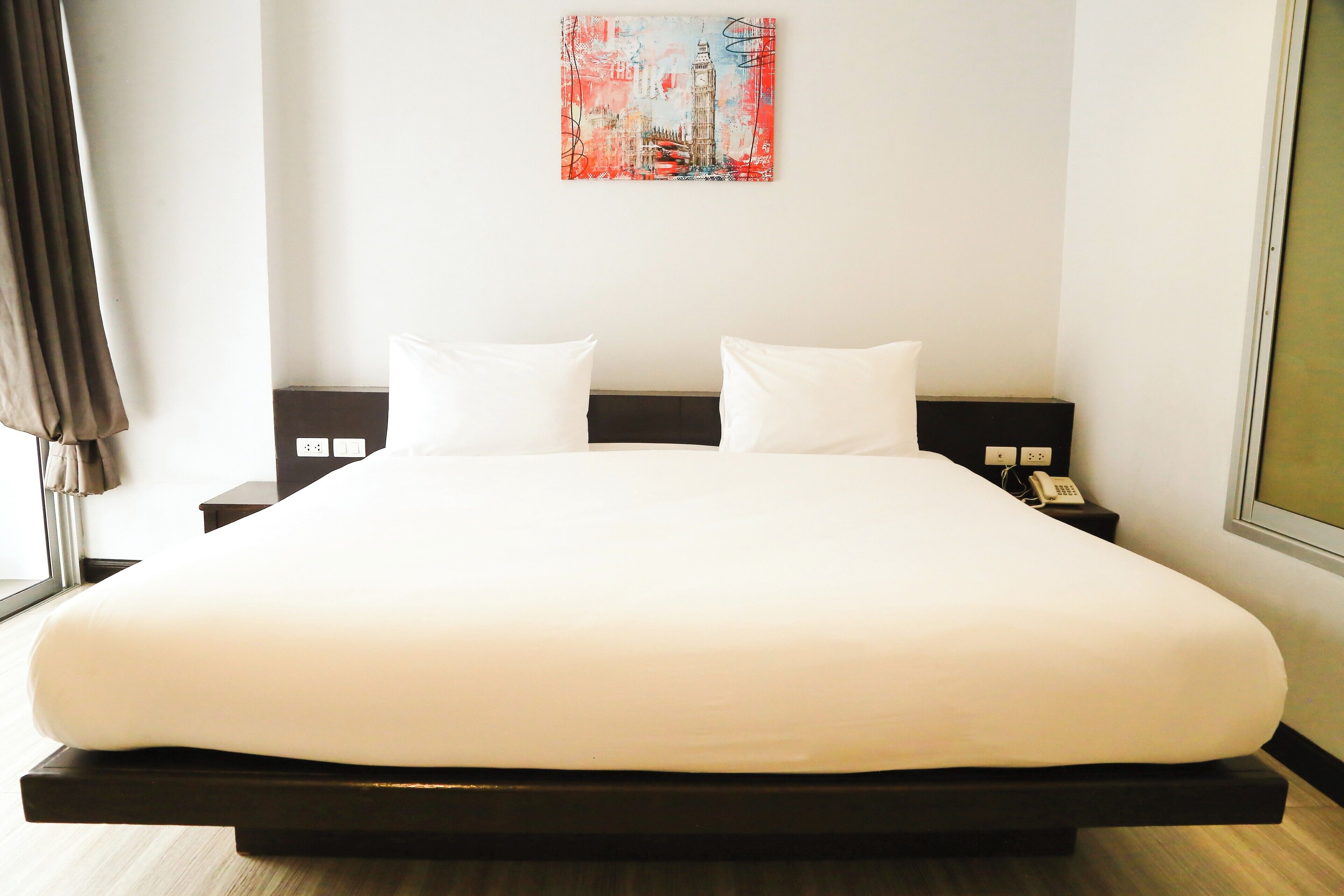Una cama grande con ropa de cama blanca, un cabecero negro y un cuadro de un paisaje urbano en la pared.