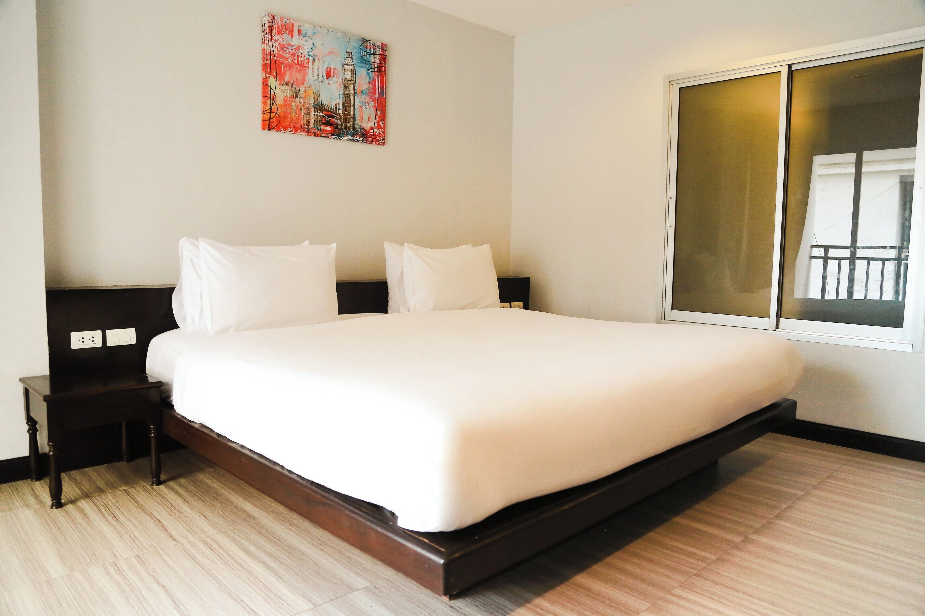 A large bed with white linens, a small bedside table, and a wall-mounted painting.
