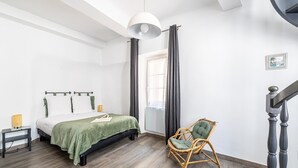 A bedroom with a bed, a chair, a nightstand, a lamp, and a window with curtains.