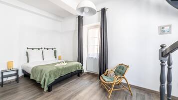 Une chambre à coucher avec un lit, une chaise, une table de chevet, une lampe et une fenêtre avec des rideaux.