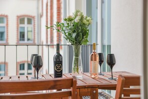 Une table en bois, avec des verres à vin, des bouteilles et un vase de fleurs, sur un balcon.