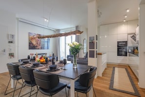 Une cuisine moderne avec des meubles blancs, un four encastré et un coin repas comprenant une table en bois foncé et des chaises noires.