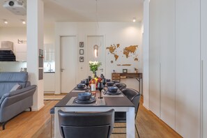 Uma sala de jantar moderna com uma mesa comprida posta para quatro pessoas, um sofá cinza e um mapa-múndi na parede.