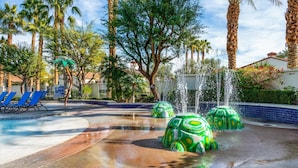 A water feature with green turtle sculptures, a pool with blue tiles, and palm trees.