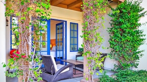 A covered outdoor seating area with wicker furniture, a blue door, and greenery.