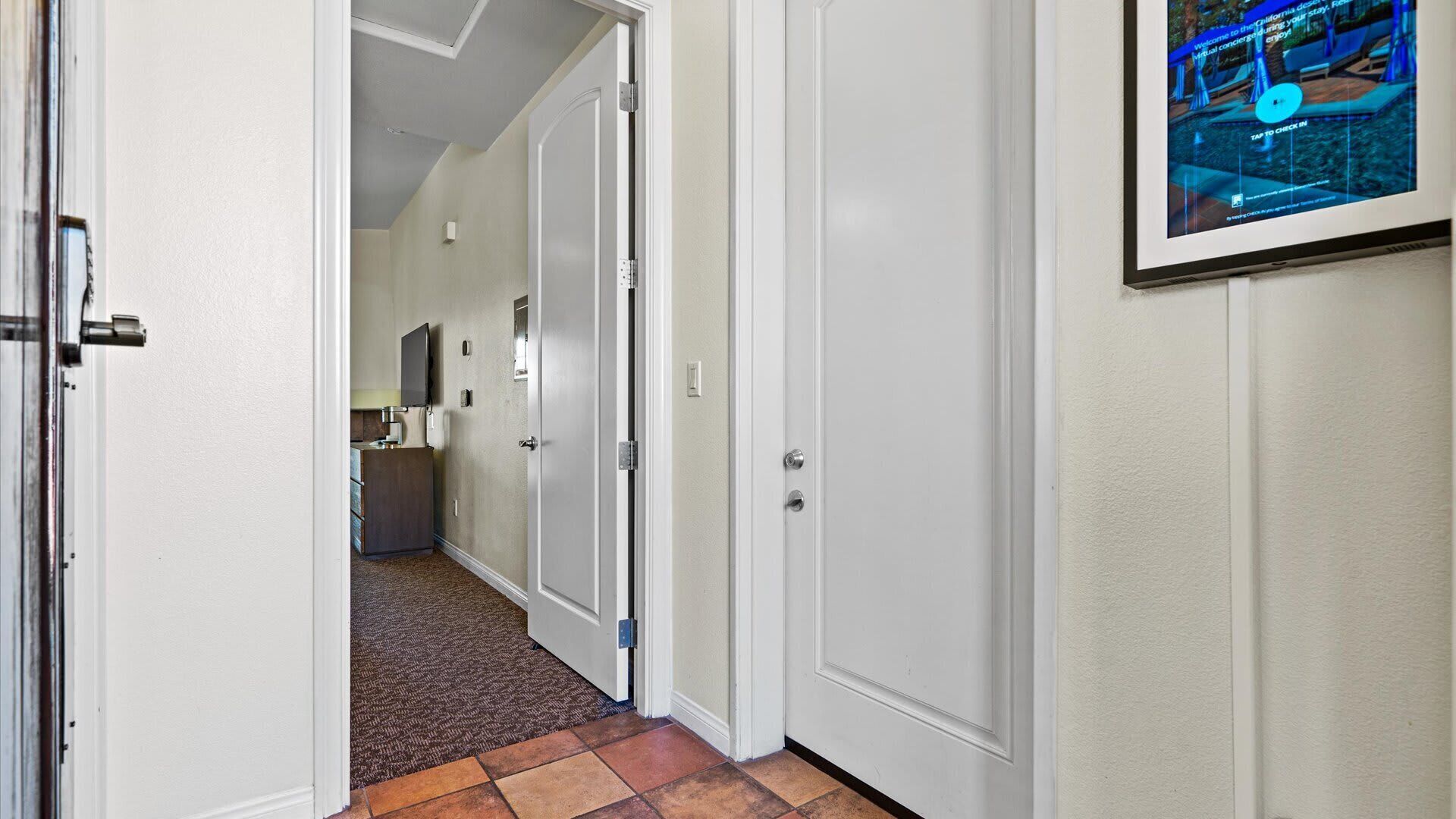 A hallway with a carpeted floor, white walls, and a door leading to a room with a desk and a chair.