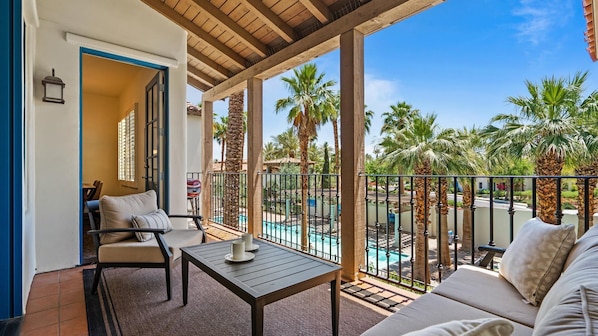A balcony with a pool, palm trees, and a view of the surrounding area.