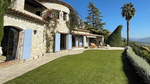 A stone building with a curved roof, a well-maintained lawn, and a view of the mountains. - Villa Bougainvilliers (Vence)