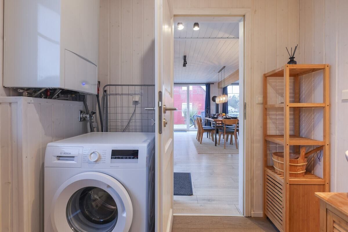 A laundry room with a Bosch washing machine, wooden shelves, and a dining area in the background.