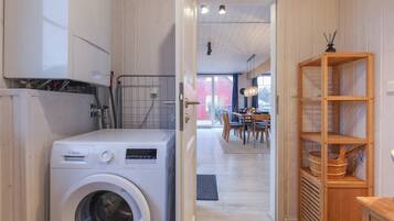 A laundry room with a Bosch washing machine, wooden shelves, and a dining area in the background.