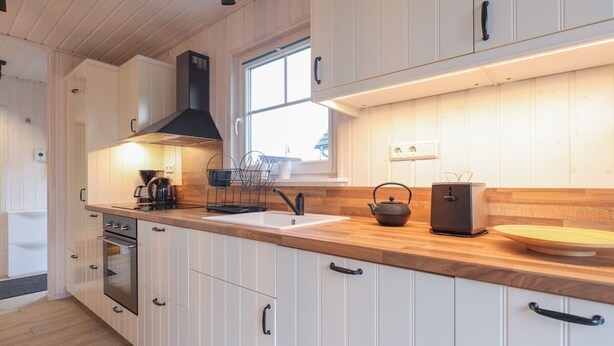 Une cuisine moderne avec des meubles blancs, un plan de travail en bois, une cuisinière et une fenêtre qui laisse entrer la lumière naturelle.