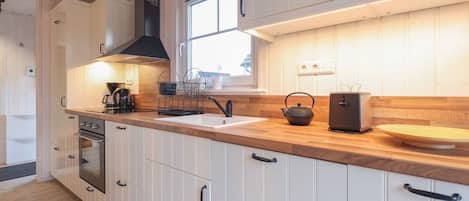 A modern kitchen with white cabinets, a wooden countertop, a stove, and a window providing natural light.