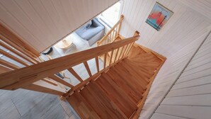 Un escalier en bois mène à un niveau inférieur, d’où l’on peut voir un canapé et une affiche accrochée au mur.