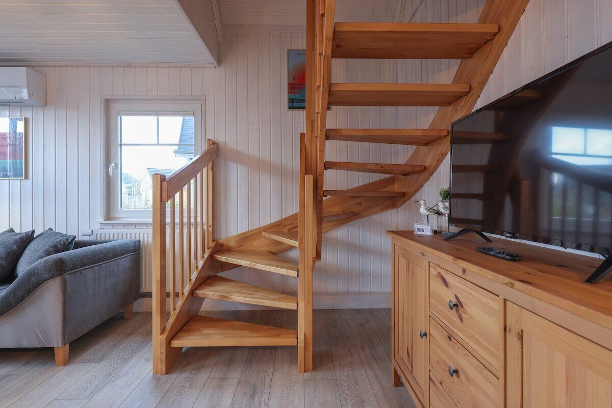 A wooden staircase leading to an upper level, a grey sofa, a wooden cabinet, and a television on the right.