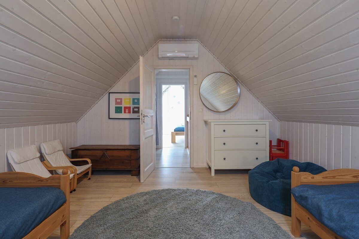 A cozy attic bedroom with two wooden beds, a blue bean bag, a white dresser, and a round mirror on the wall.