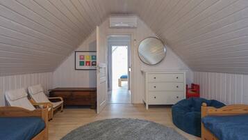 A cozy attic bedroom with two wooden beds, a blue bean bag, a white dresser, and a round mirror on the wall.