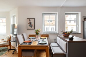 A modern kitchen with a dining area, featuring a wooden table, chairs, a fruit bowl, and a television.