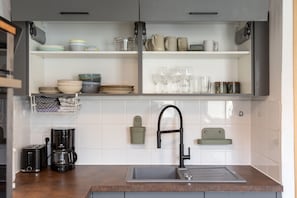A kitchen with a stainless steel sink, a coffee maker, and various dishes and glasses on shelves.