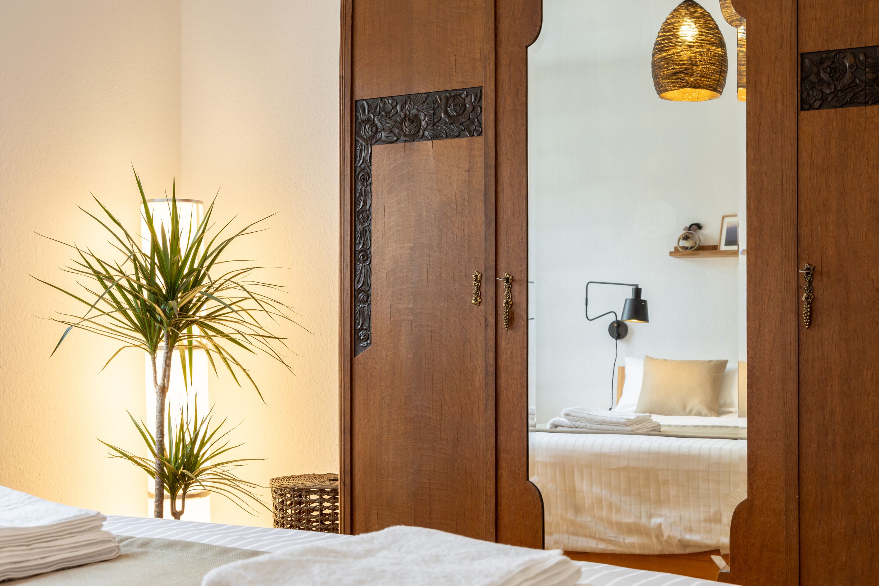 A hotel room with a bed, a bedside lamp, a potted plant, and a wooden door with a decorative frame.