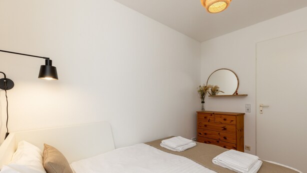 Un dormitorio con cama, lámpara de noche, cómoda y espejo.