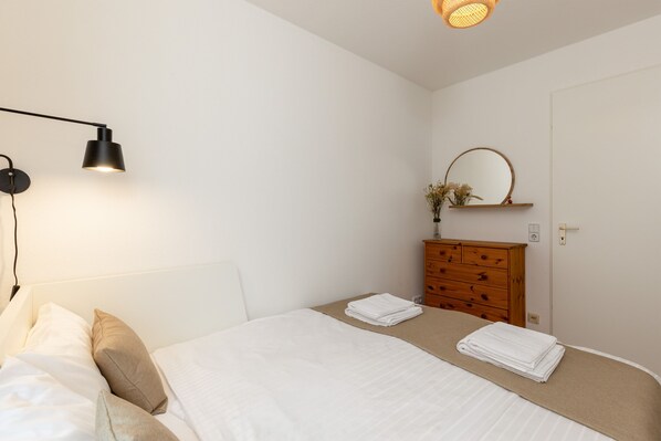 A bedroom with a bed, a bedside lamp, a dresser, and a mirror.