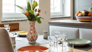 A dining table set with plates, glasses, and cutlery, a vase with flowers, and a fruit bowl on the counter. - 3 rooms apartment- 4 people (Leipzig)