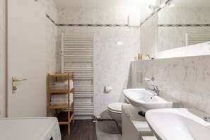 Een moderne badkamer met een wit wastafelmeubel, spiegel en toilet. Er is een houten plank met handdoeken en een radiator.