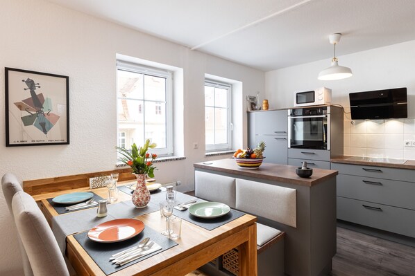 Una cocina moderna con zona de comedor, que incluye una mesa de madera, sillas y una isla integrada con un cuenco de fruta.