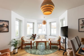 A modern living room with a round table, two chairs, a TV, and a large window.