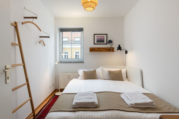 A neatly arranged bedroom with a bed, a wooden ladder, a window, and a wall-mounted shelf.