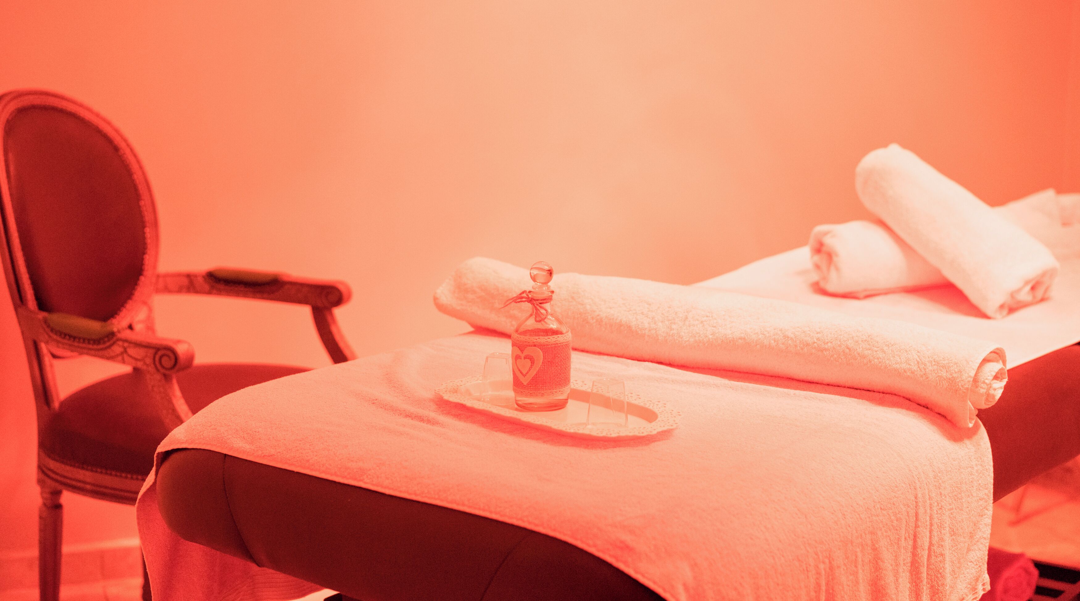 A room with a bed, a chair, and a bottle of lotion on a tray.