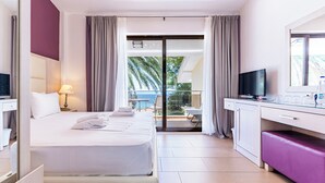 Een hotelkamer met een bed, een bureau, een televisie en een balkon met uitzicht op palmbomen.
