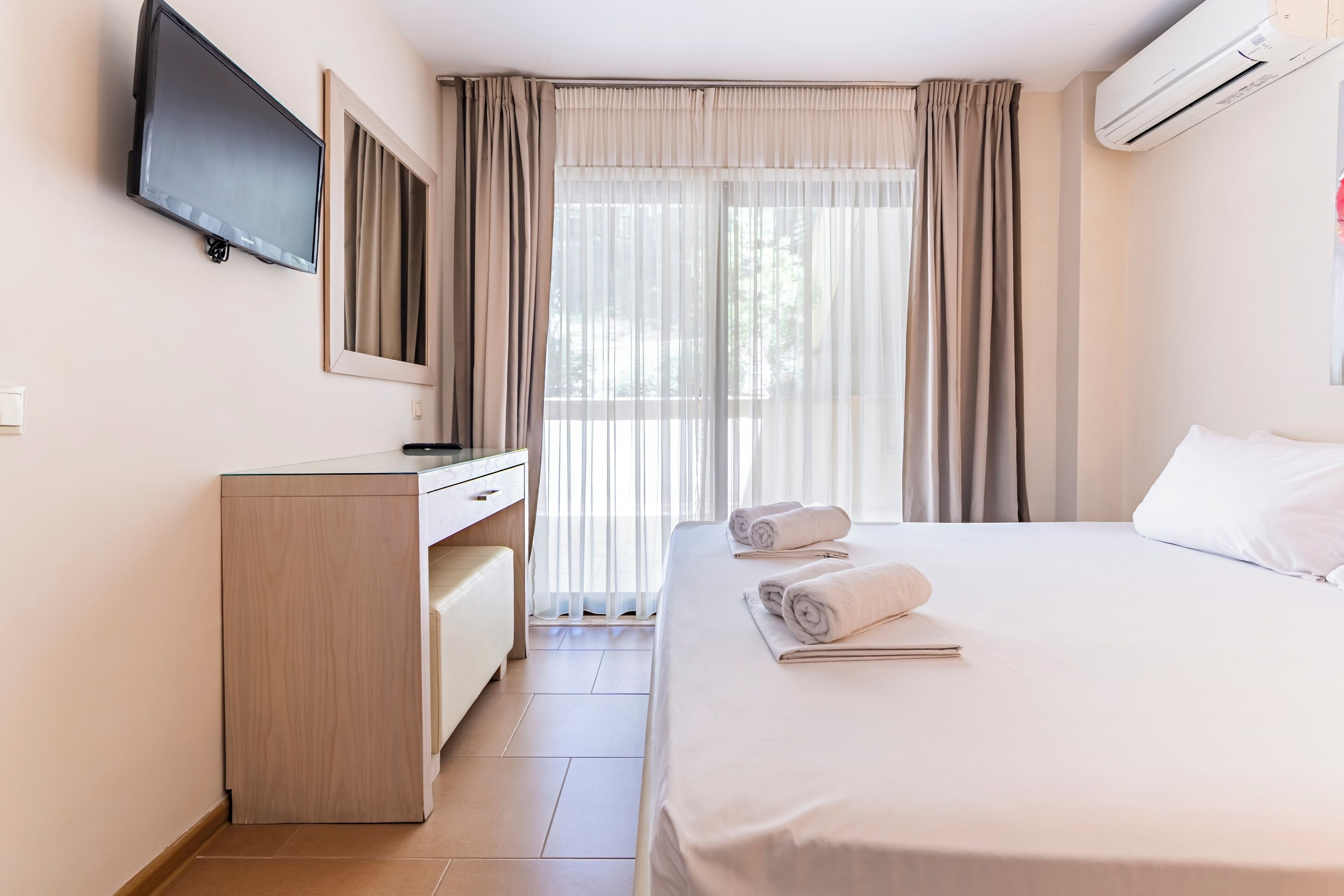 A hotel room with a bed, a desk, a TV, and an air conditioning unit.