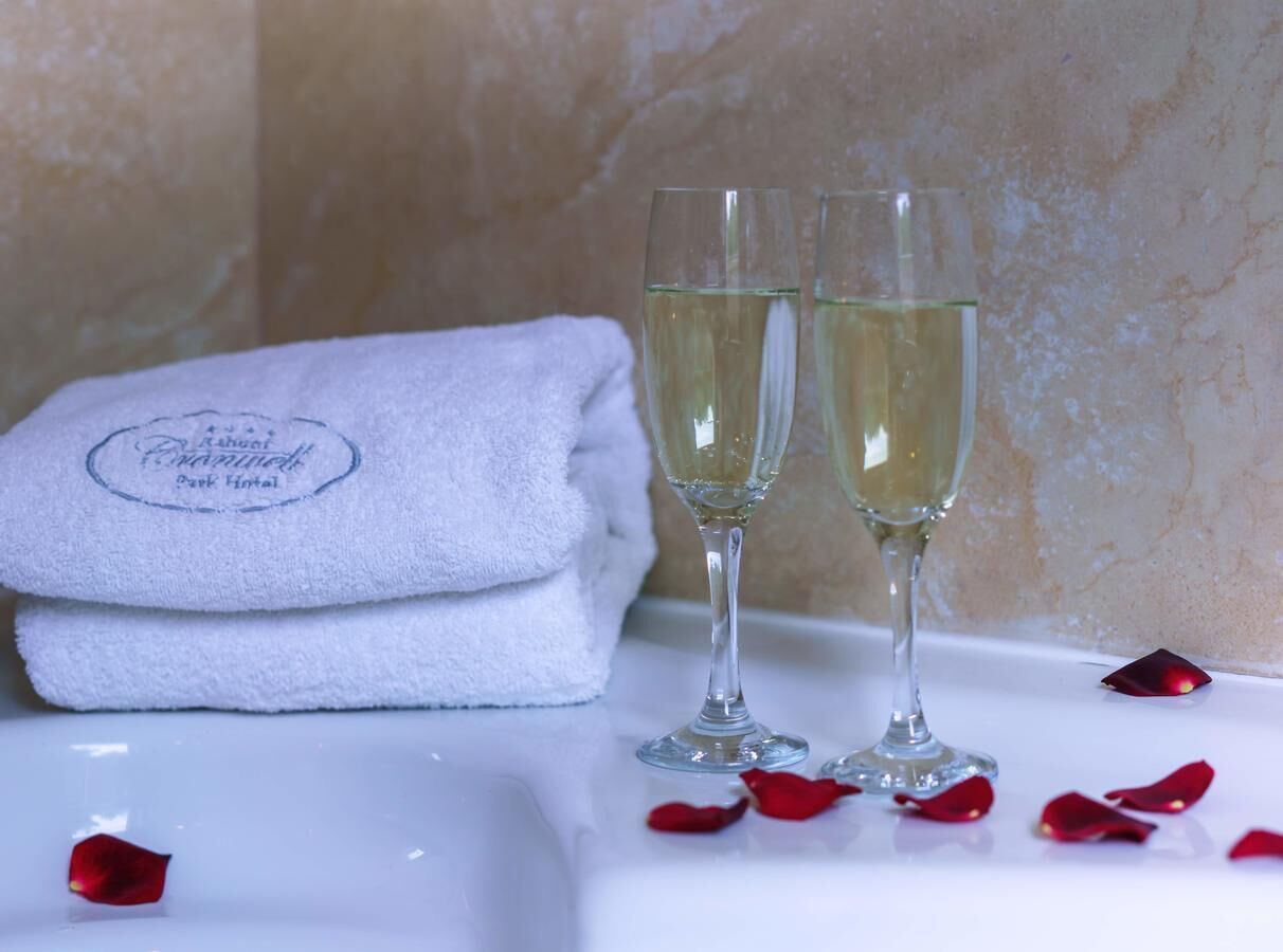 A white bathroom with a towel and two glasses of white liquid, possibly champagne, on a marble surface.