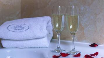 A white bathroom with a towel and two glasses of white liquid, possibly champagne, on a marble surface.
