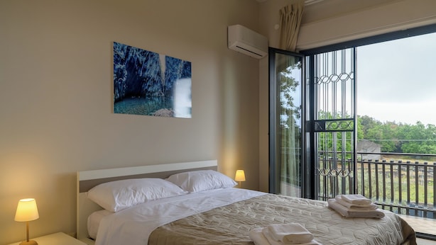 Habitación de hotel con una cama grande, dos lámparas de noche, un cuadro de una cascada y un balcón con vistas a la vegetación.