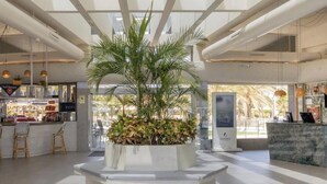 A modern lobby with a central planter, seating area, reception desk, and visible bar. - Hotiday Gran Canaria Maspalomas (San Bartolome de Tirajana)