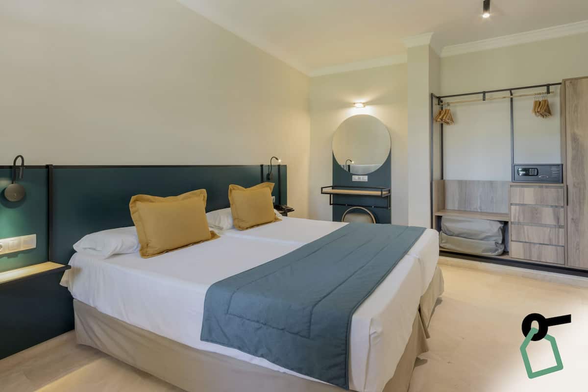 Een hotelkamer met een groot bed, twee nachtkastjes, een spiegel, een wastafelmeubel en een houten garderobe.
