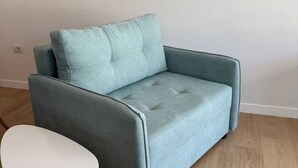 Un sofá azul claro con respaldo y reposabrazos acolchados, ubicado en una habitación con pared blanca y piso de madera.