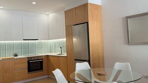 Una cocina moderna con armarios de madera, un refrigerador de acero inoxidable y una mesa de comedor de vidrio con sillas blancas.
